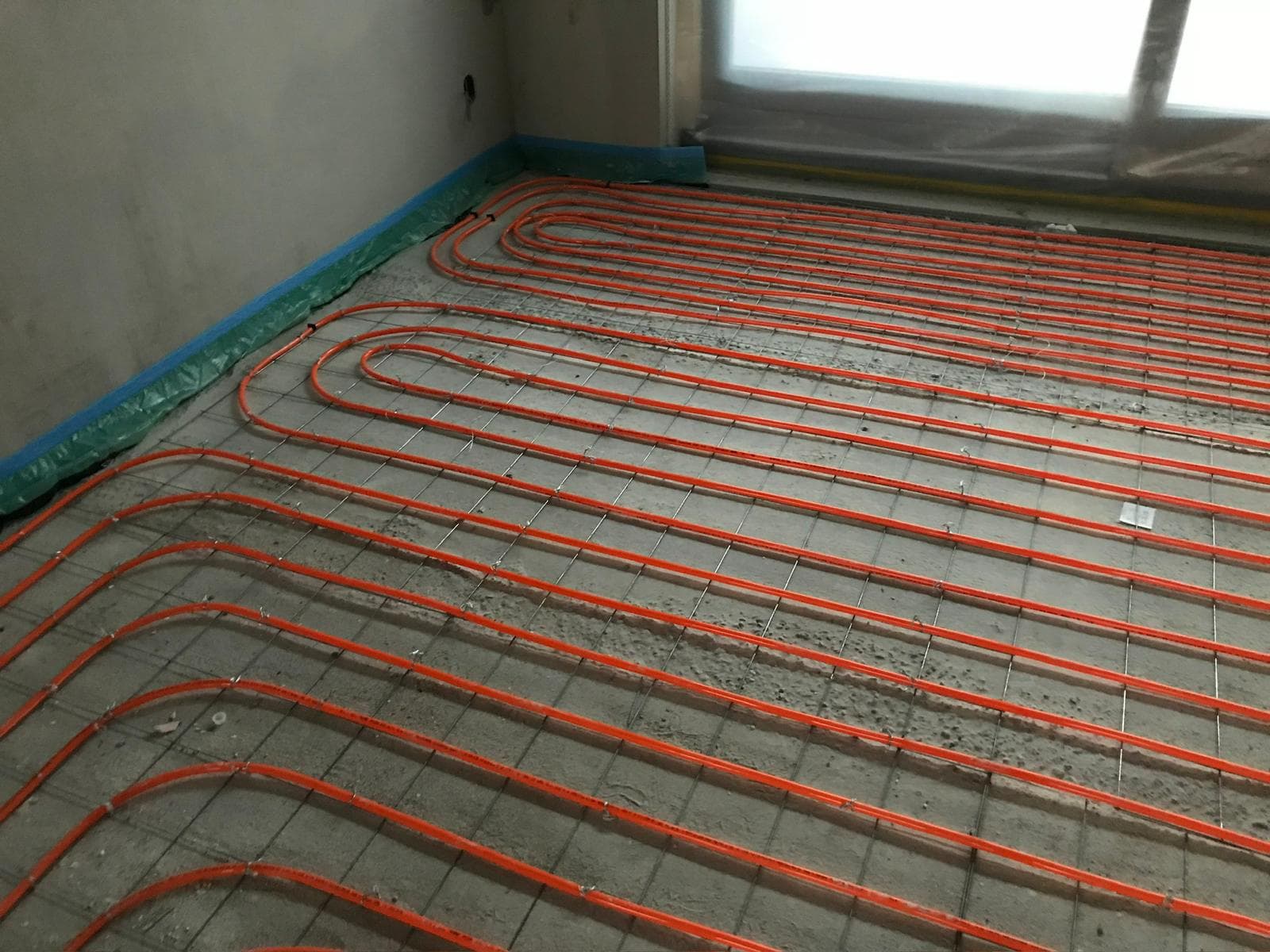 Vloerverwarming aangelegd met oranje leidingen op betonvloer