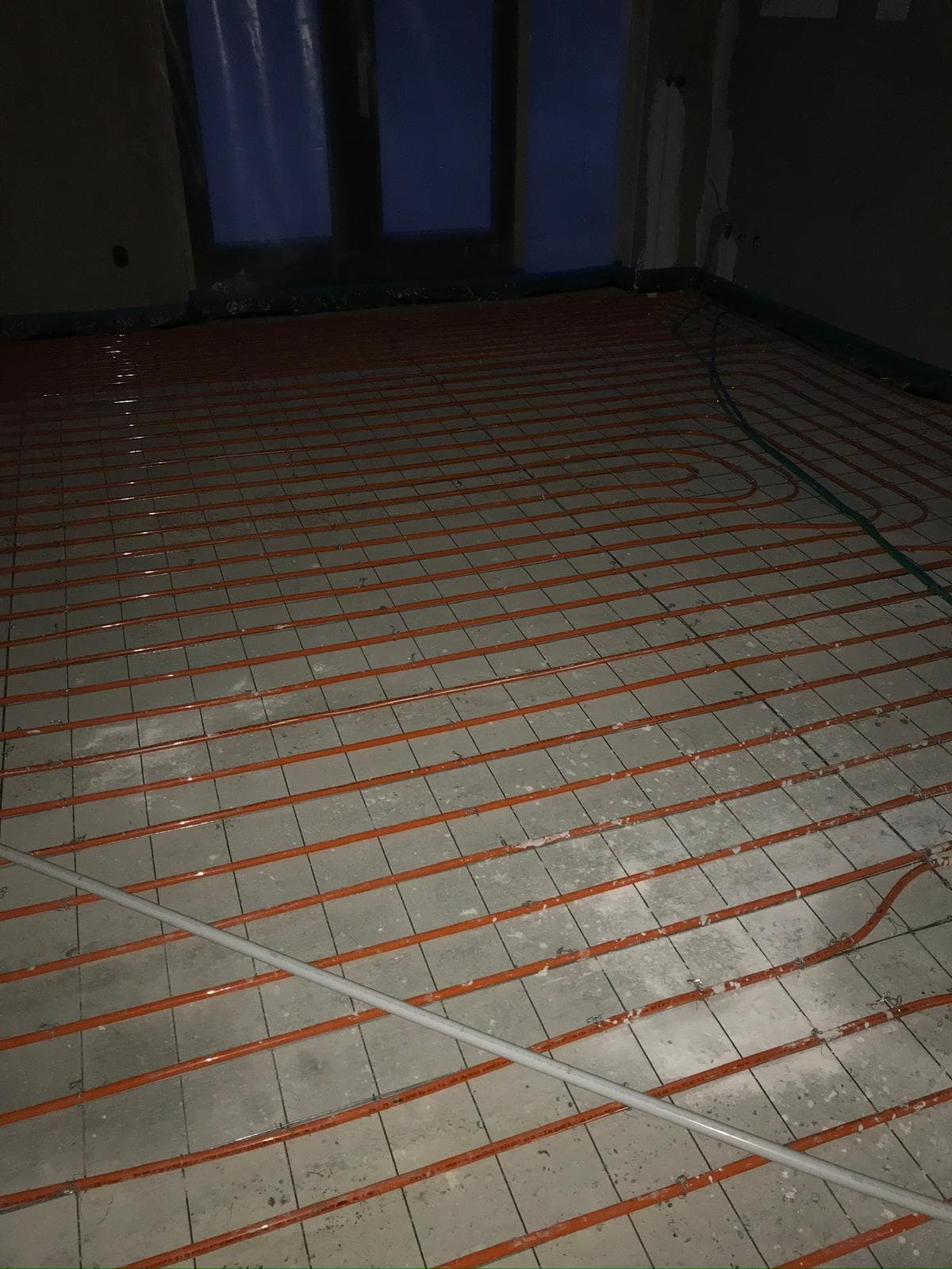 Vloerverwarming in een groot vertrek, oranje leidingen netjes in slingerpatroon gelegd