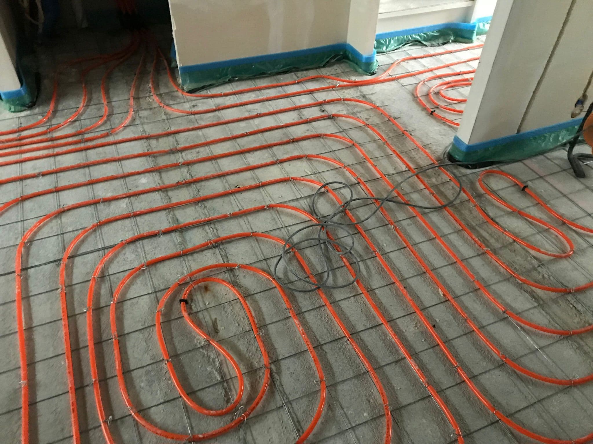 Aanleg van vloerverwarming in een groot woonvertrek, oranje leidingen op isolatieplaten